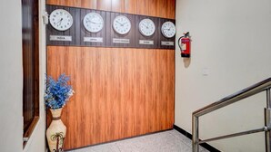 A wooden wall with clocks set to different countries, a fire extinguisher, and a vase with flowers. - Hotel maayra inn (Noida)