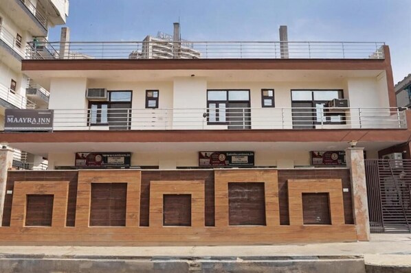 A two-story building with a flat roof, a balcony on the upper floor, and a gated entrance.