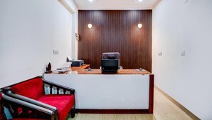 A reception area with a wooden reception desk, a red sofa, and a laptop on the desk. - Hotel maayra inn (Noida)