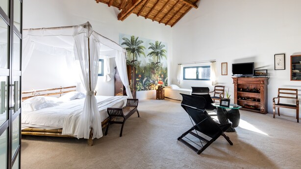 A bedroom with a four-poster bed, a desk with a chair, a television, and a wooden cabinet.