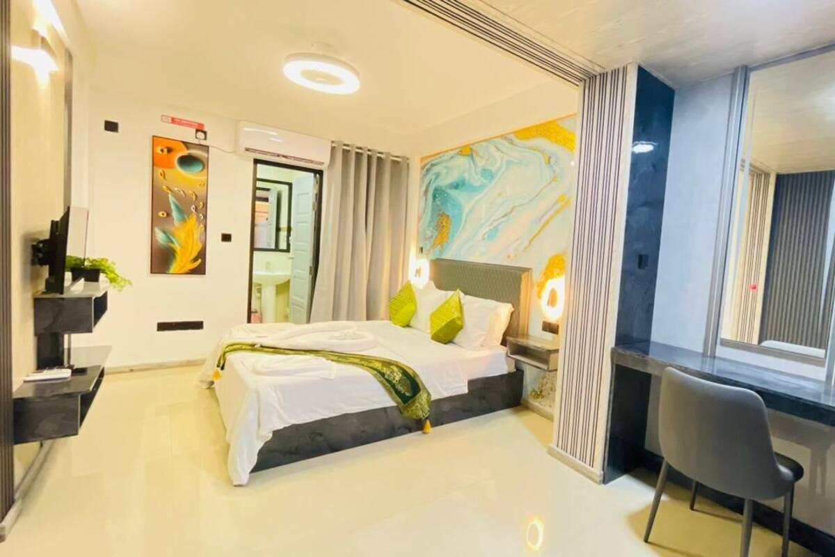 Una habitación de hotel moderna con cama, mesita de noche, silla y un ventanal grande.