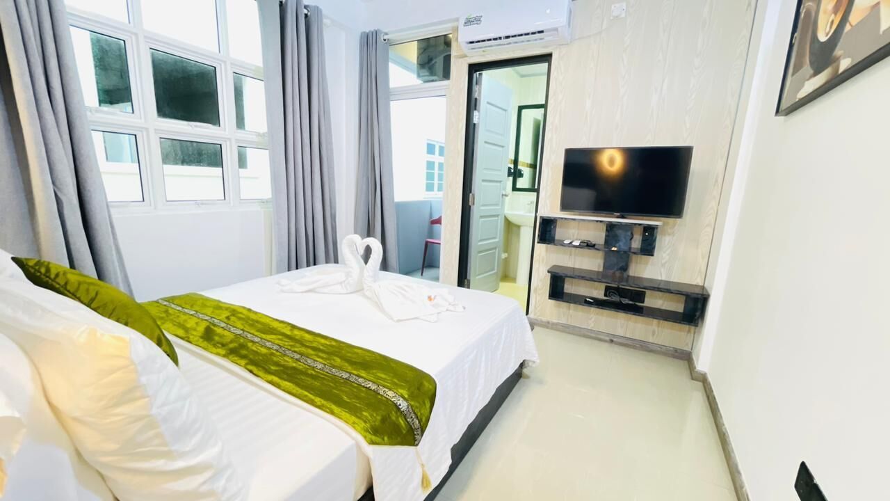A hotel room with a bed, a TV, and a bathroom visible through an open door.