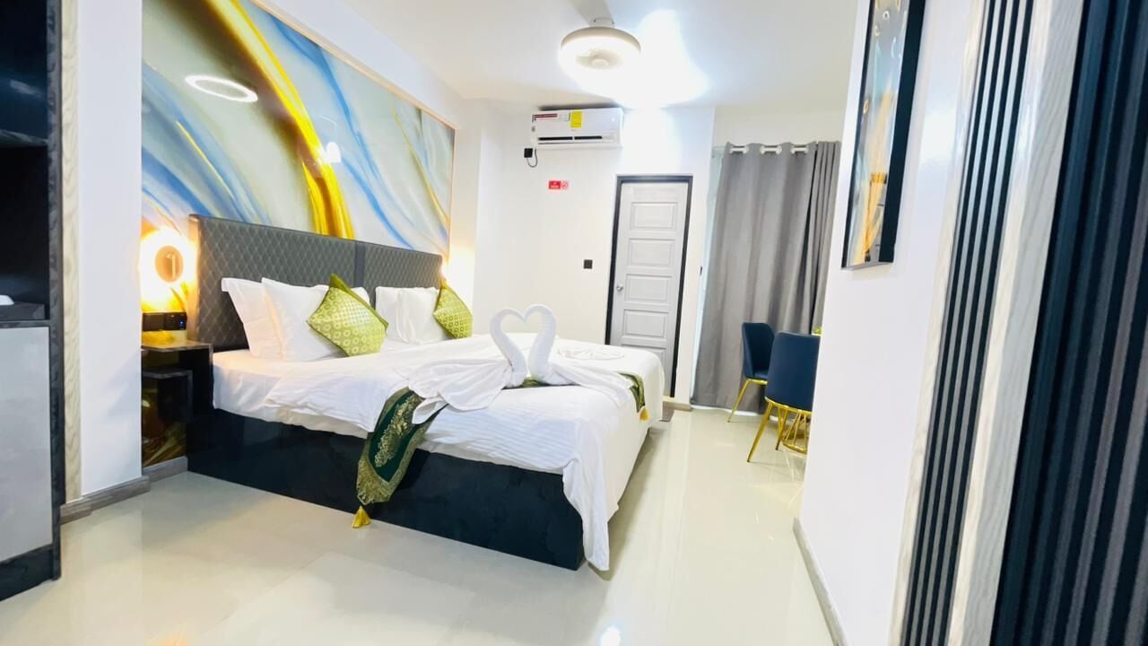 Una habitación de hotel moderna con una cama grande, una mesita de noche, aire acondicionado de pared y una puerta.