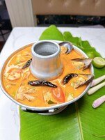 Un bol de sopa de mariscos con una taza de metal en el centro, servido sobre una hoja verde.