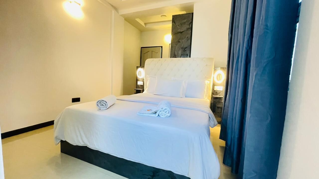 A neatly made bed with a white bedspread and pillows, a bedside table with a lamp, and a large mirror on the wall.