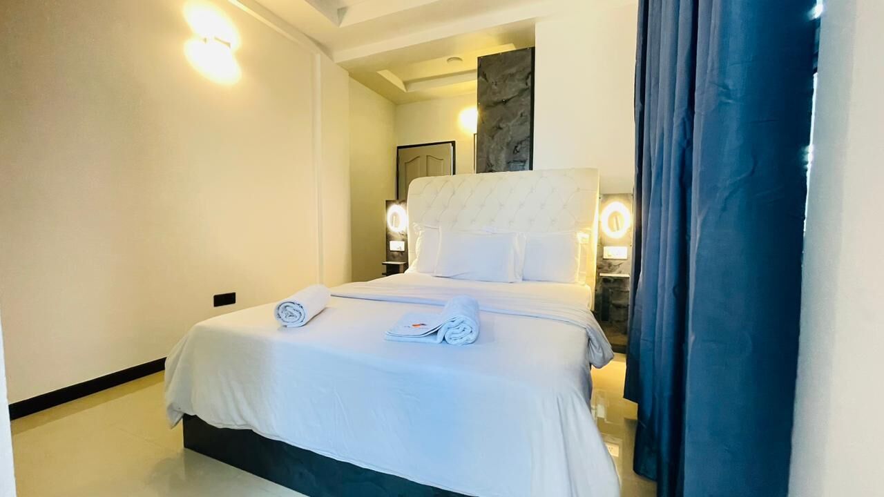 A hotel room with a bed, a nightstand, a mirror, and a wall-mounted light fixture.
