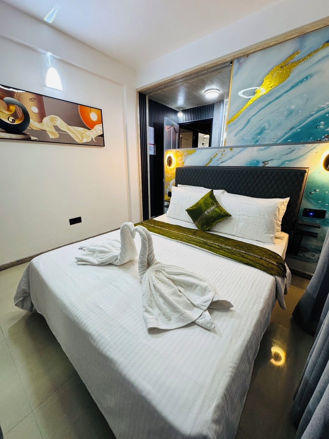 Une chambre d’hôtel avec un lit bien fait, un grand tableau au mur et une tête de lit moderne.