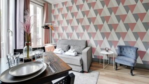 A modern living room with a grey sofa, a blue armchair, a dining table with plates and glasses, and a geometric patterned wall. - Peaceful Studio - 2P -near the Canal Saint-martin (Paris)