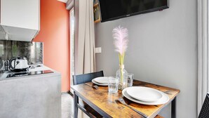 A dining area with a wooden table set for two, a vase with a pink feather, and a flat-screen TV mounted on the wall. - Peaceful Studio - 2P -near the Canal Saint-martin (Paris)