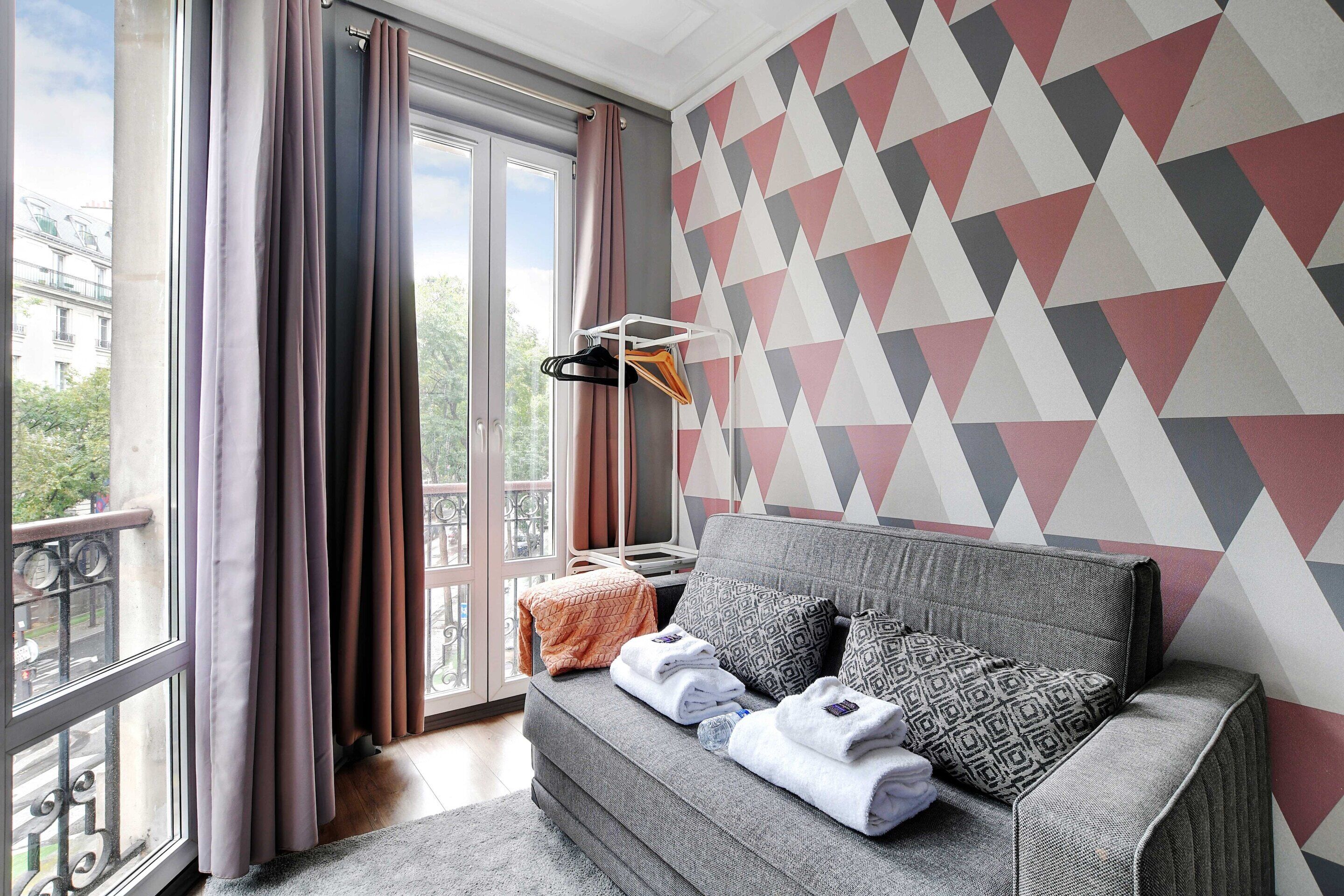 A modern room with a grey sofa, patterned cushions, and a geometric wall design.
