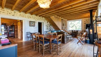A rustic interior with a wooden dining table, chairs, a staircase, and a stone wall.