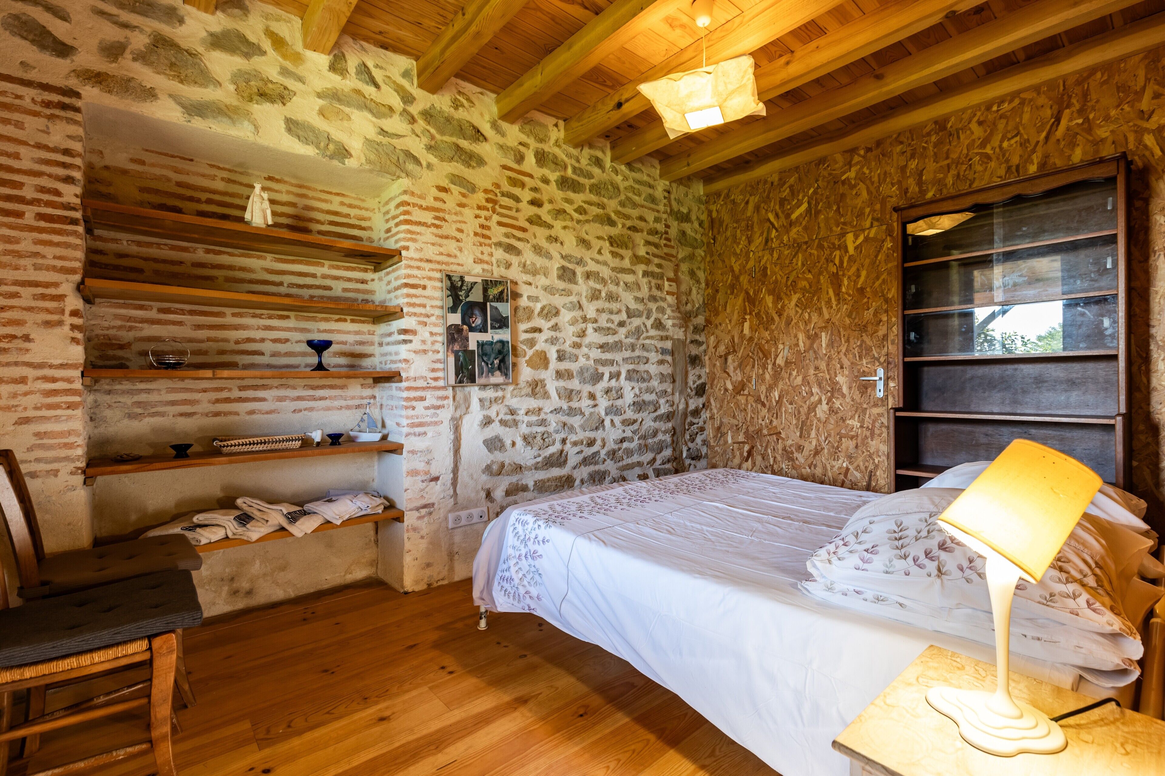 Een eenvoudige kamer met een bed, houten planken, een stoel en een lamp.