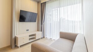 Una sala de estar moderna con un televisor de pantalla plana en la pared, un sofá y una ventana con cortinas traslúcidas.
