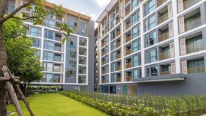 Un edificio residencial moderno de varios pisos con balcones, un césped bien cuidado y un árbol en primer plano.