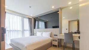 Una habitación de hotel moderna con una cama grande, un escritorio con silla, un espejo y una ventana con cortinas.