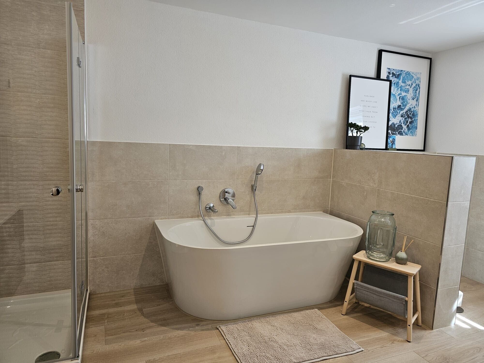 A modern bathroom with a freestanding bathtub, a glass shower enclosure, and a small wooden stool with a glass jar.