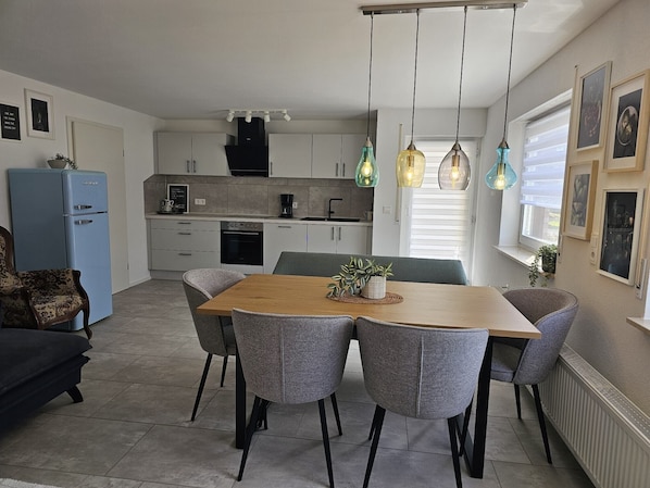 Una cocina moderna con armarios blancos, una mesa de comedor con sillas grises y lámparas colgantes.