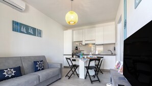 Un espacio habitable moderno con un sofá gris, una mesa de comedor con sillas, una zona de cocina y una lámpara colgante.