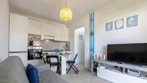 Una sala de estar moderna con sofá, televisión y cocina al fondo.