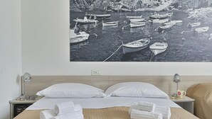 A neatly made bed with white linens, a headboard, and a wall-mounted picture of boats on water. - The Houses on the Park 2 (La Spezia)