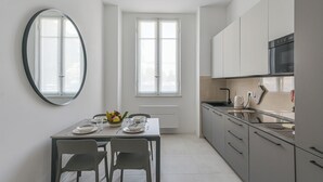 A modern kitchen with a dining table set for two, a large mirror, and a window providing natural light. - The Houses on the Park 2 (La Spezia)