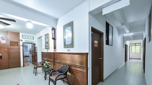 Ein Empfangsbereich mit einer Rezeption, zwei Korbstühlen, einer Uhr und einer Tür mit der Aufschrift 'Office'.