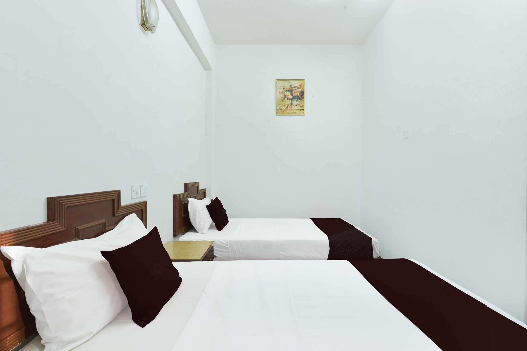 A hotel room with two beds, white bedding, dark brown headboards, and a single wall-mounted light fixture.