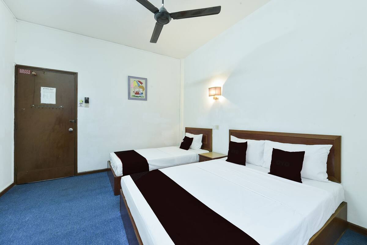 Ett hotellrum med två separata sängar, en takfläkt, en dörr med en skylt och en väggmonterad lampa.