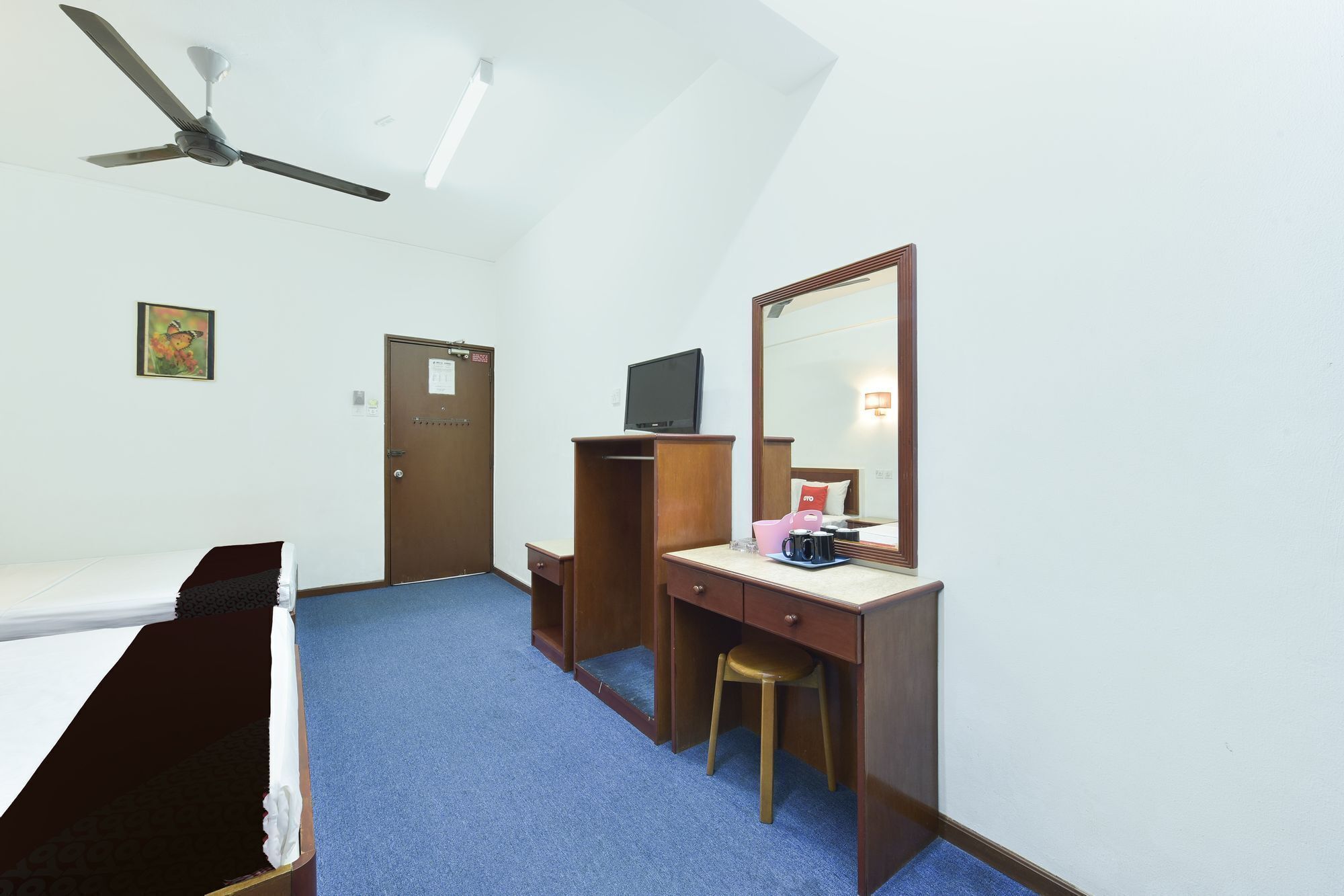 Habitación de hotel con cama, escritorio con silla, televisión, espejo y ventilador de techo.