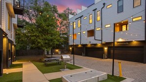 A modern building with a paved courtyard, outdoor seating, and a barbecue grill.