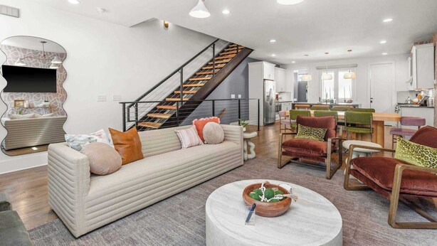 A modern living room with a sofa, coffee table, and chairs. A staircase leads to an upper level.