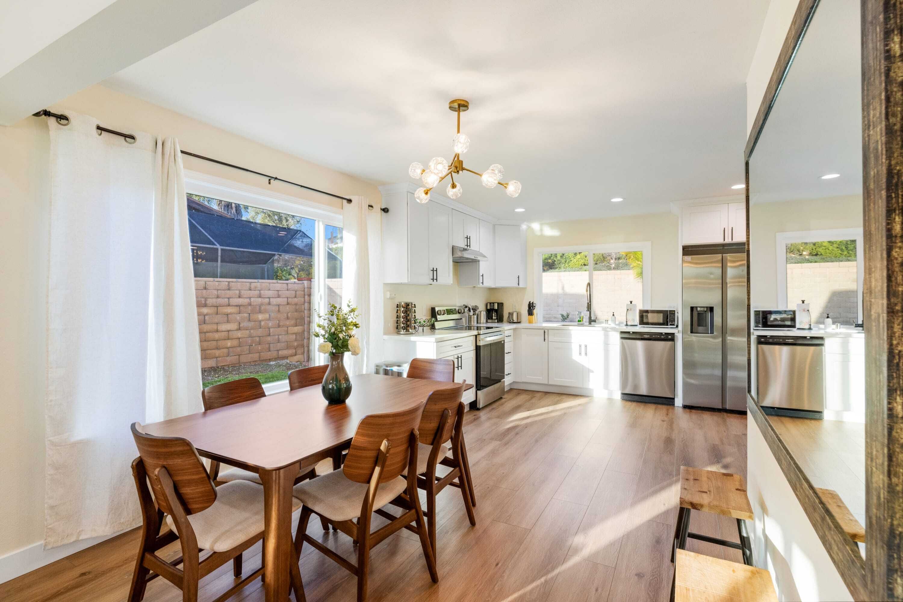 A modern kitchen with white cabinets, stainless steel appliances, and a wooden dining table with chairs.