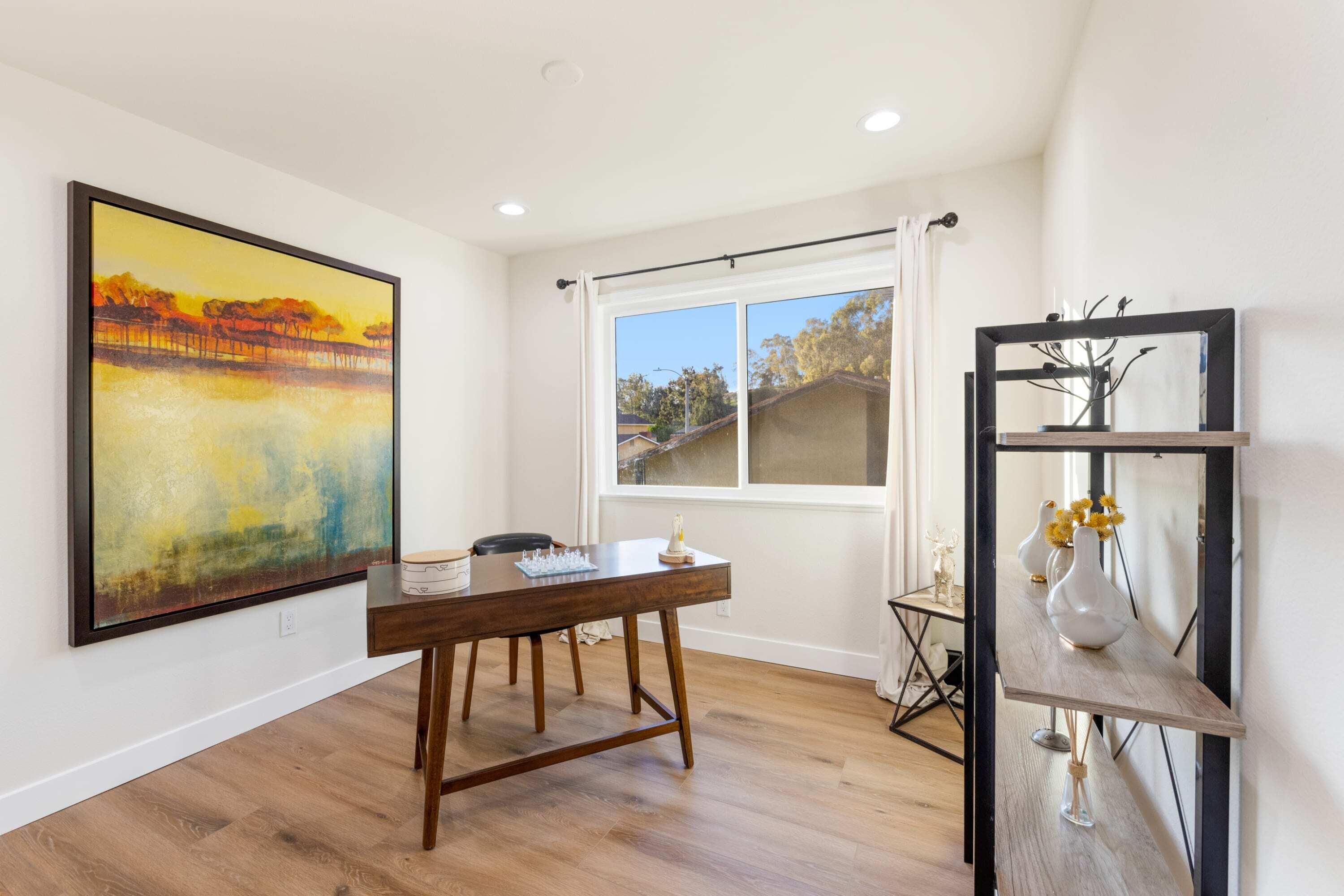 A dining area with a wooden table, a painting on the wall, and a window with curtains.