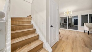 A staircase leading to a room with a white door, a chandelier, and a view of a dining area.