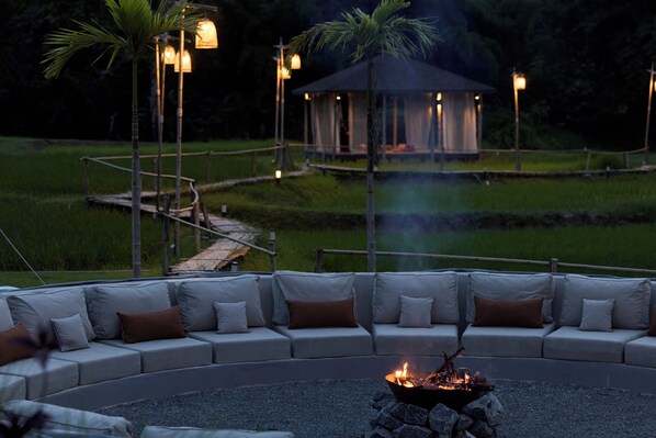A circular outdoor seating area with a fire pit, surrounded by a wooden deck and a small gazebo in the background. - Tantawan Tented Camp, Chiang Rai (Mae Chan)