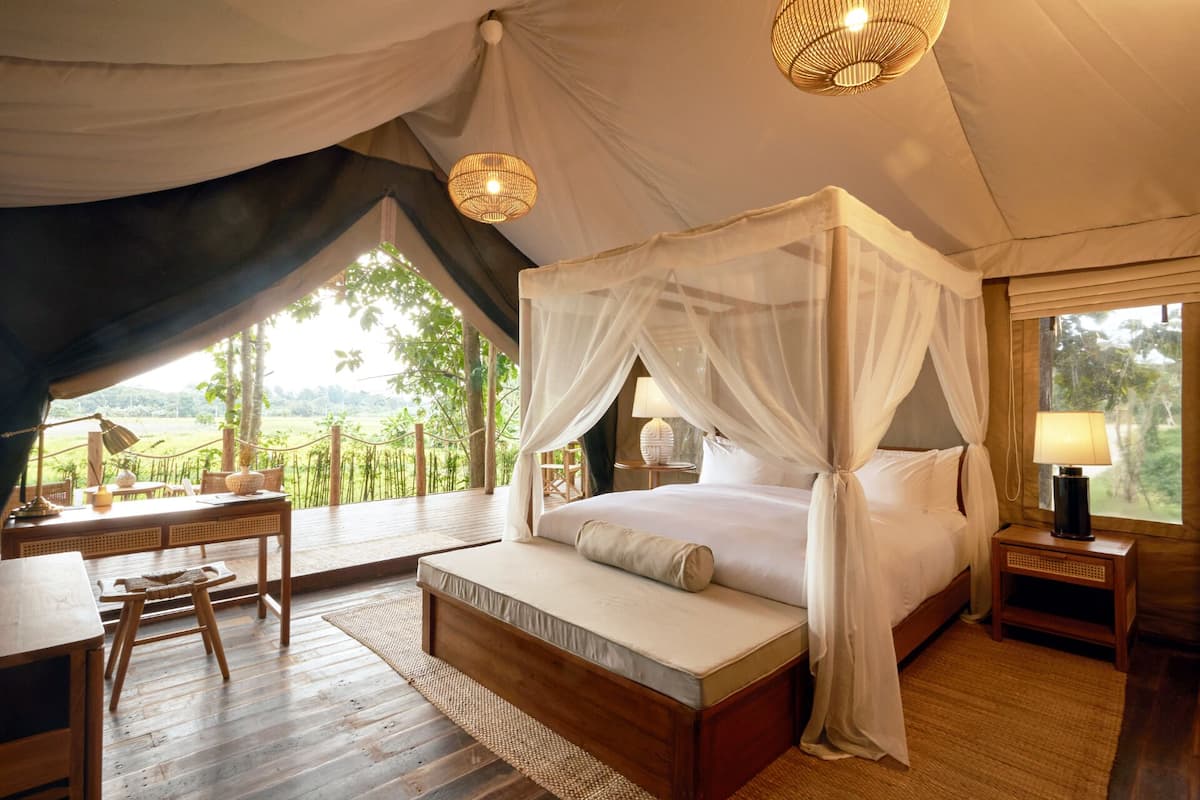 A spacious tented room with a four-poster bed, a wooden desk, and a view of the surrounding landscape.