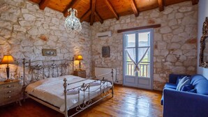 Une chambre avec un mur en pierre, un plafond en bois, un cadre de lit en métal, un canapé bleu et une fenêtre donnant sur un paysage.