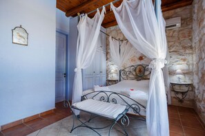 Un dormitorio con cama con dosel, una mesita de noche con lámpara y una pared de piedra.