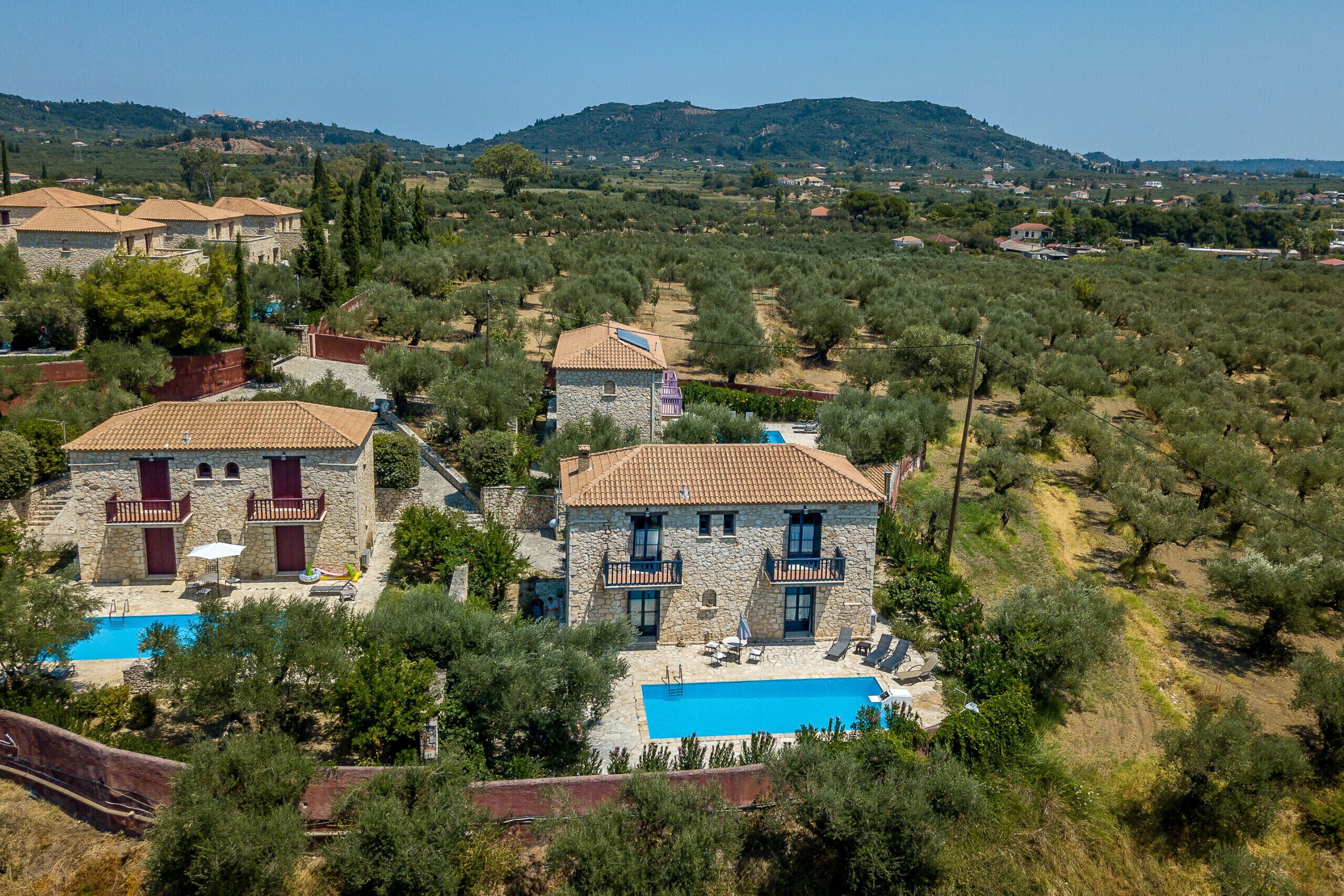 Una villa in pietra con piscina, circondata da ulivi e colline.