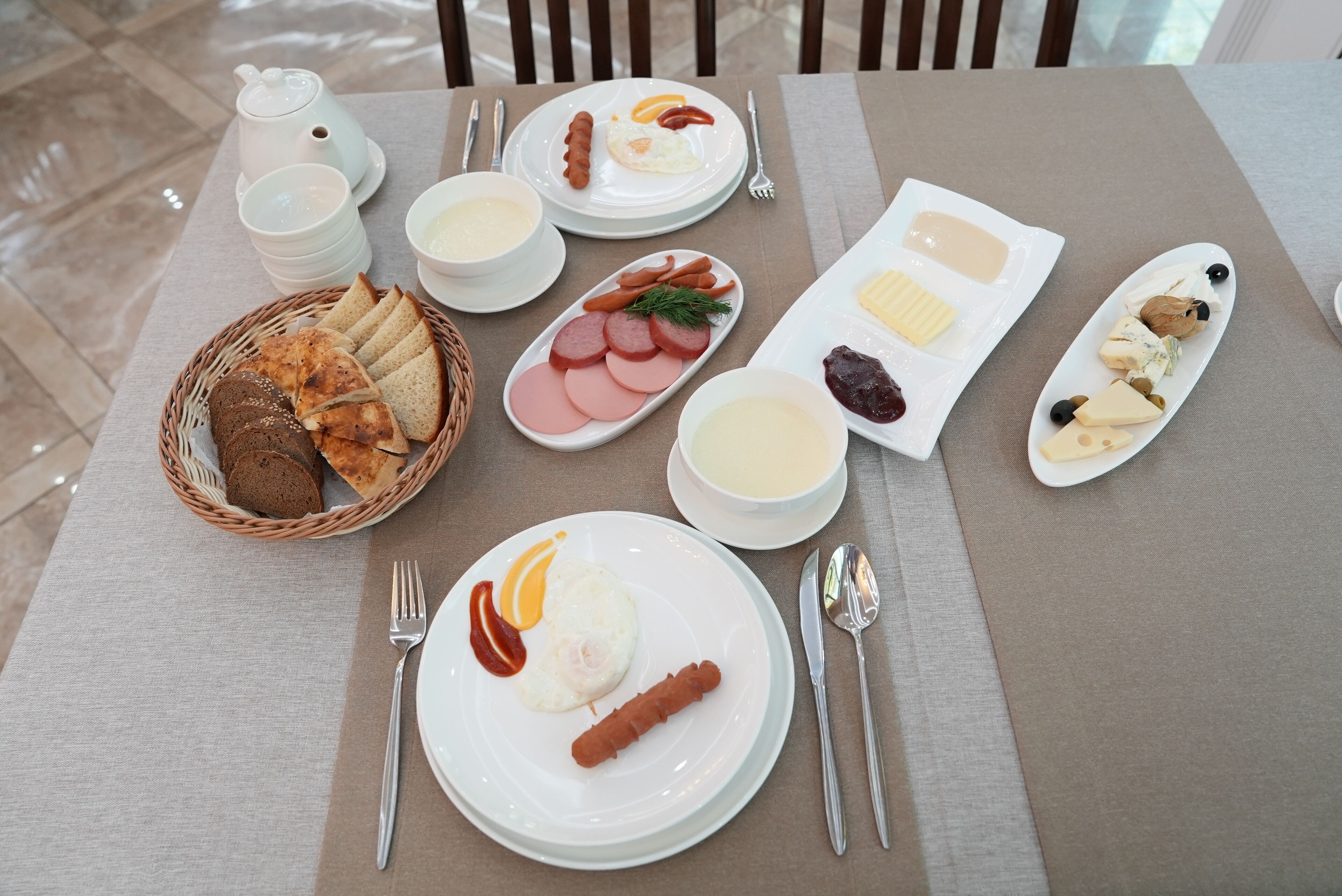 A breakfast table with various dishes including bread, eggs, sausages, and cheese.