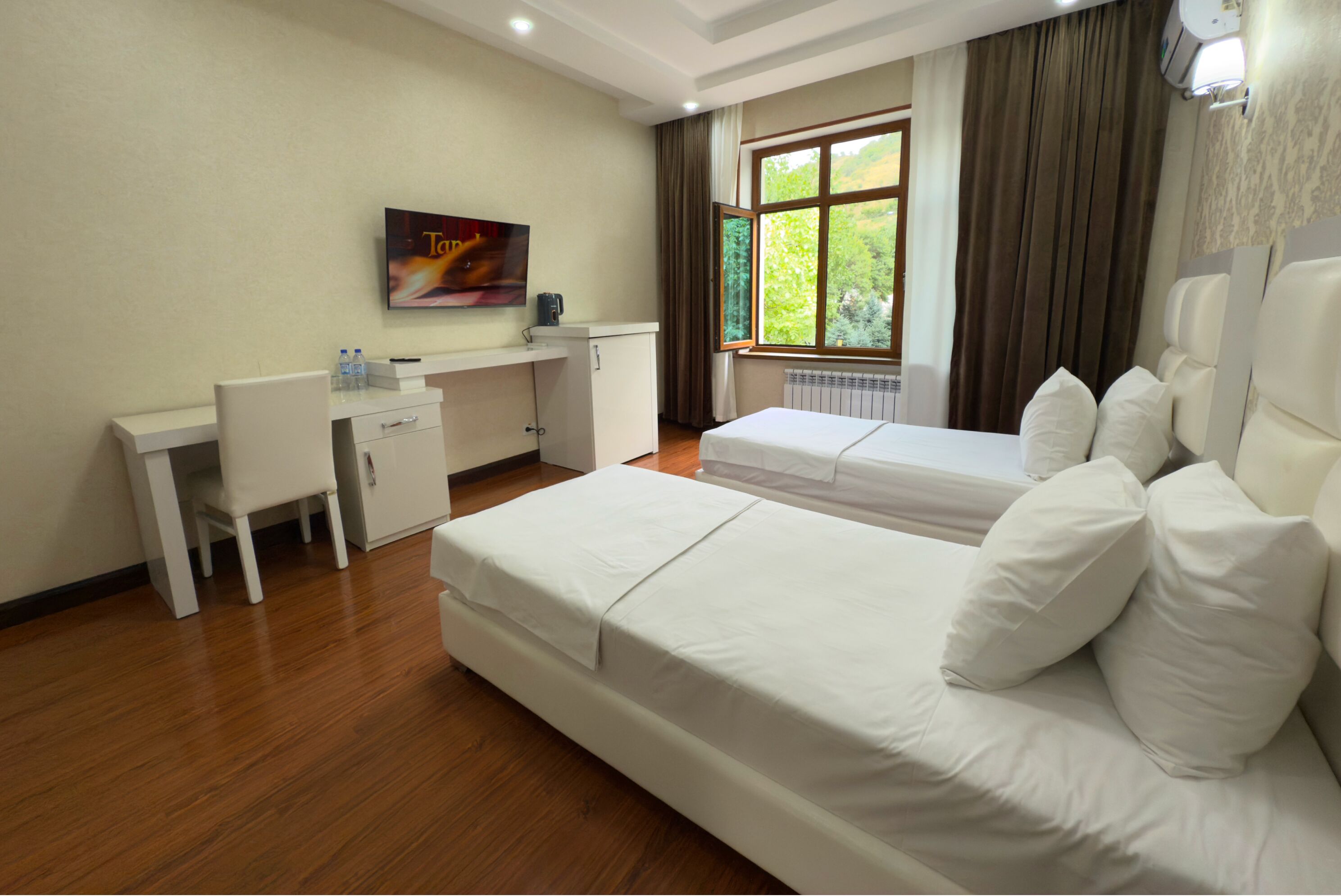 Habitación de hotel con dos camas, un escritorio, una silla, un televisor y una ventana con cortinas.