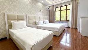 Habitación de hotel con dos camas, un ventanal con cortinas, un radiador y un aire acondicionado instalado en la pared.