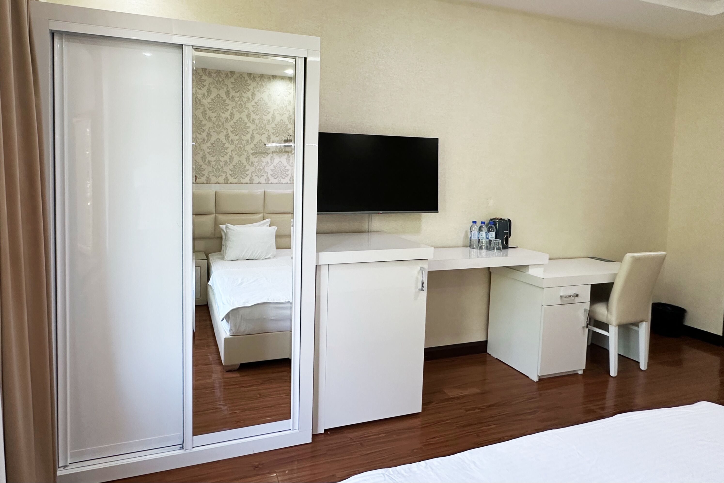 A hotel room with a bed, a desk, a chair, a TV, and a wardrobe.