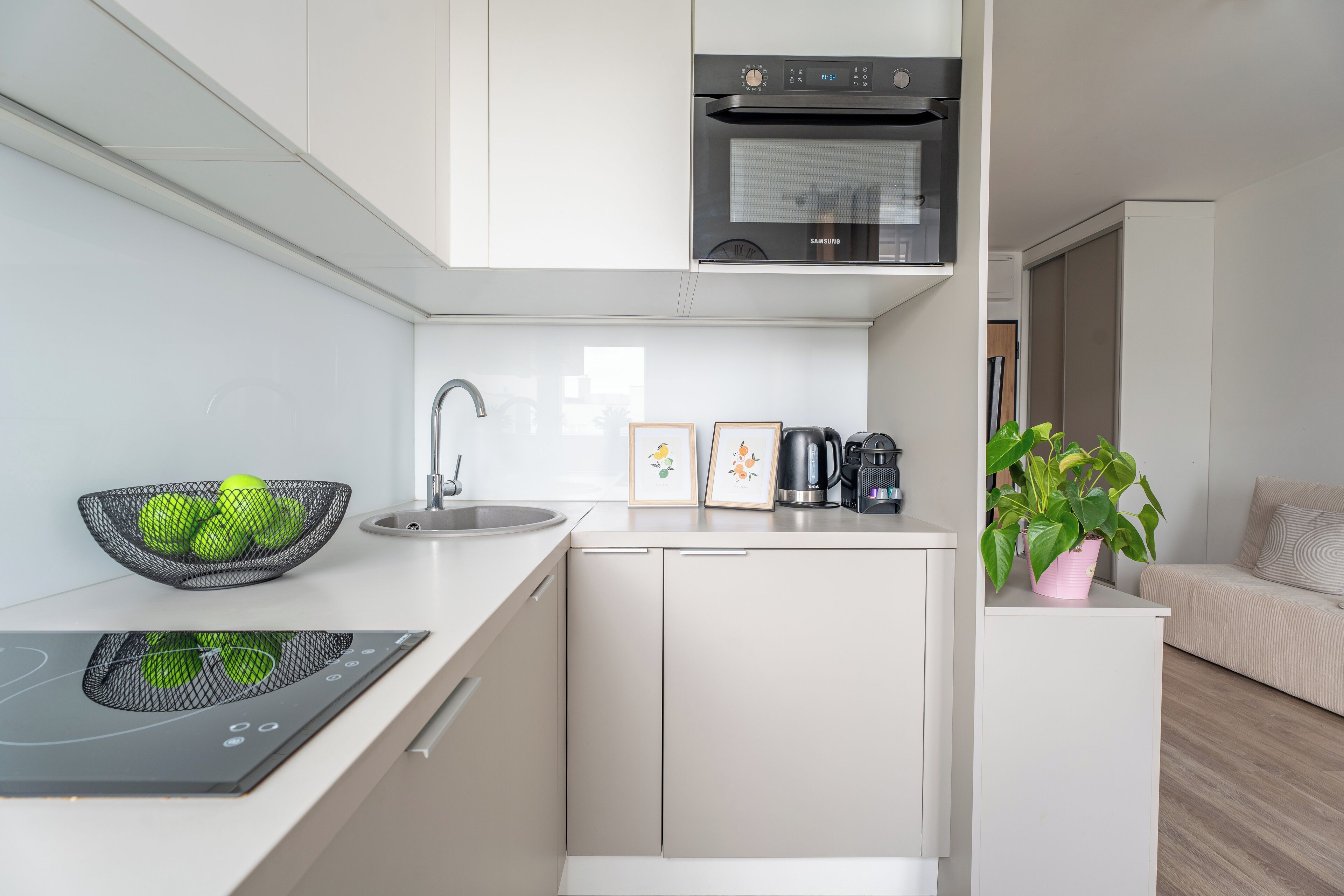 A modern kitchen with a built-in oven, a sink, and a countertop with a kettle and a coffee maker.