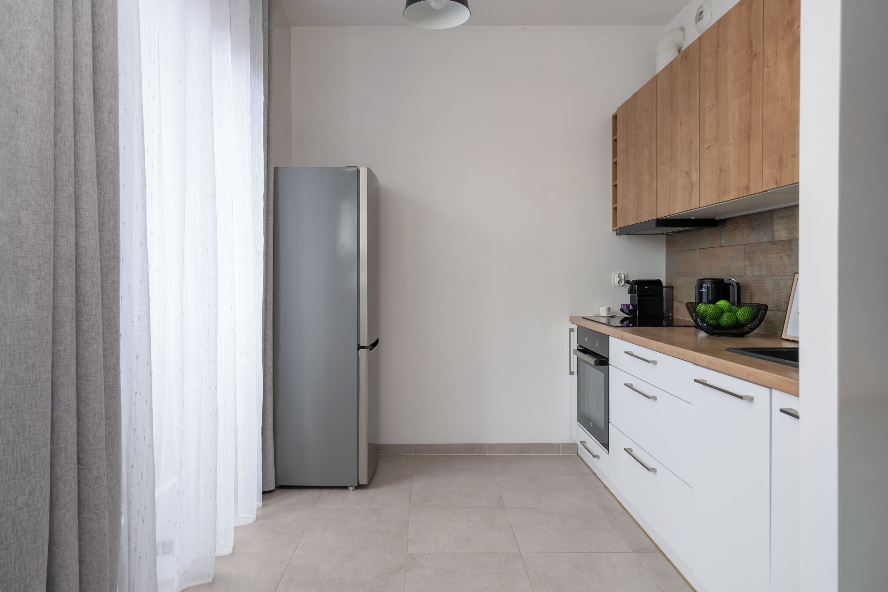 A modern kitchen with a stainless steel refrigerator, wooden cabinets, and a tiled backsplash.