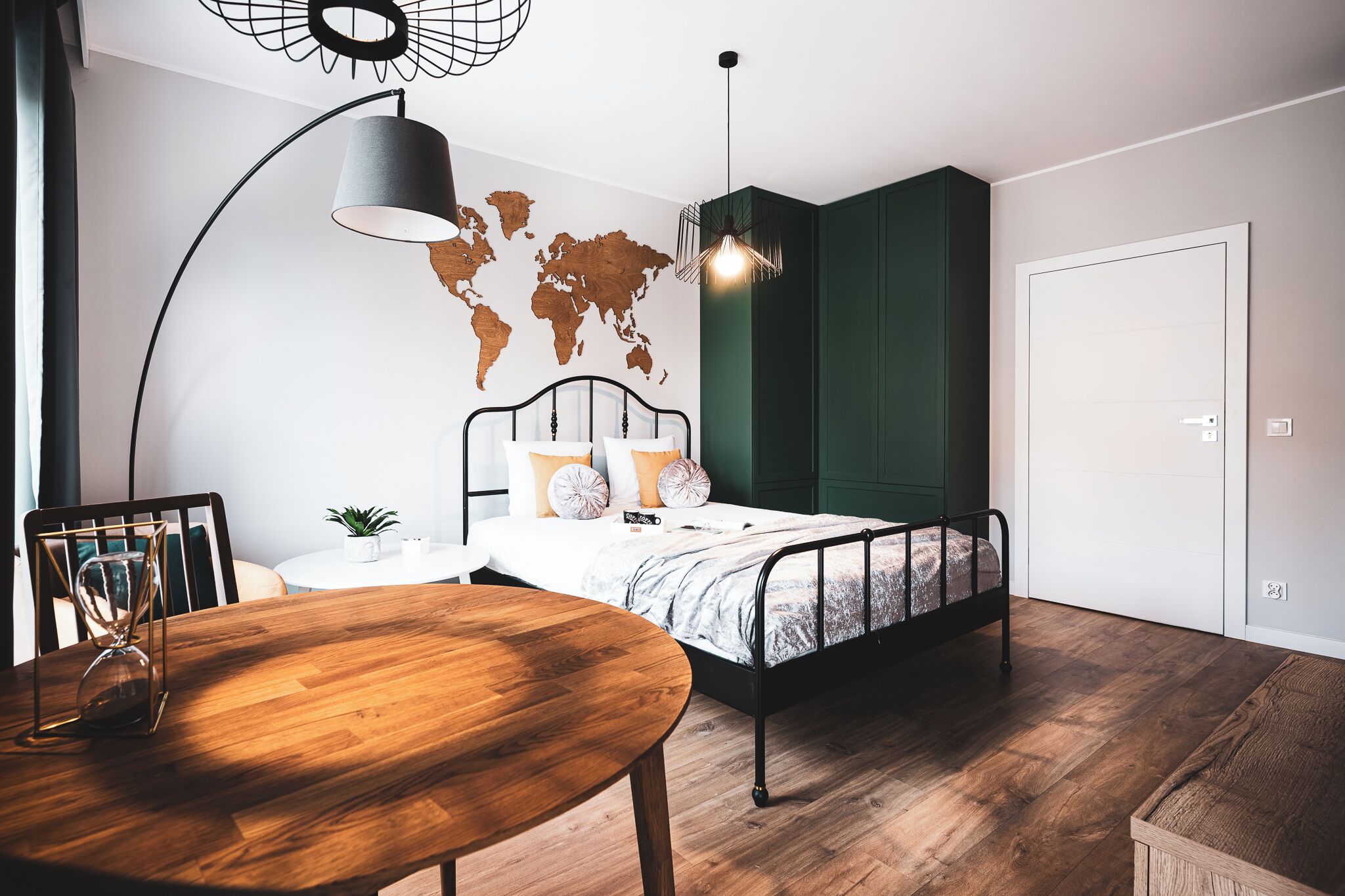 A modern bedroom with a bed, a round wooden table, a world map on the wall, and a hanging light fixture.