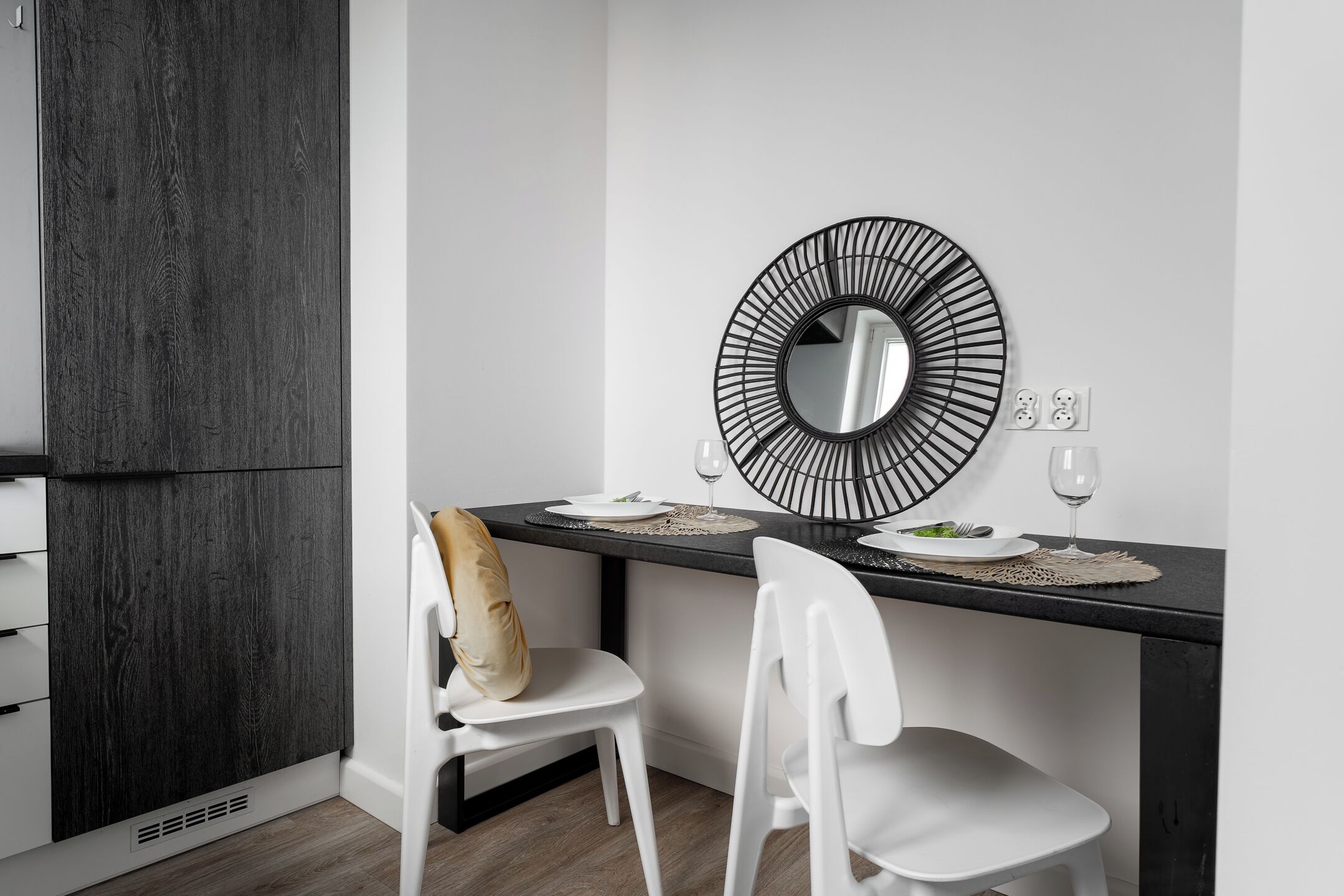 A modern dining area with a black metal mirror, white chairs, and a dark wooden cabinet.