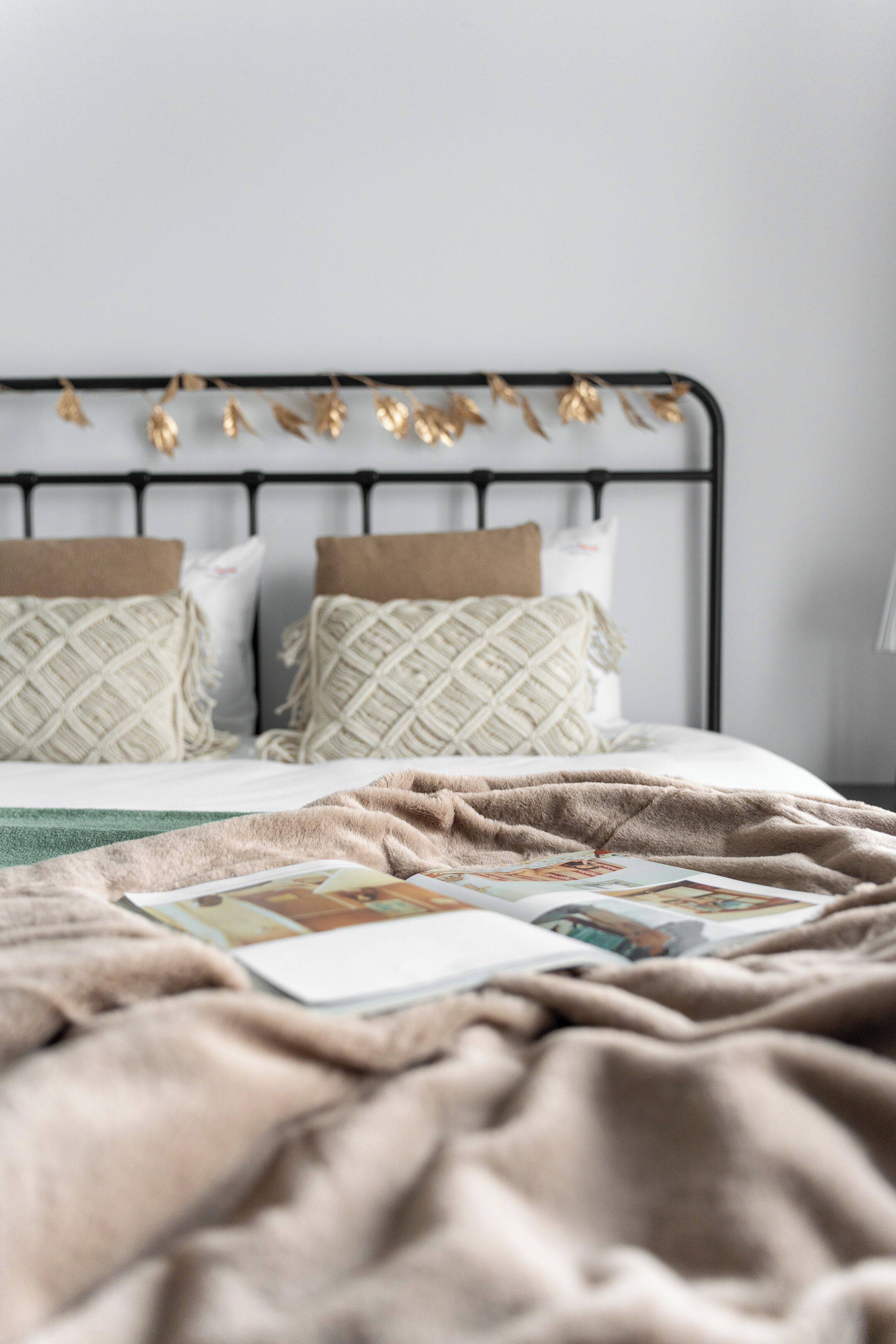 Una cama con un edredón y almohadas estampadas, una mesita de noche con un libro y una lámpara fijada en la pared.