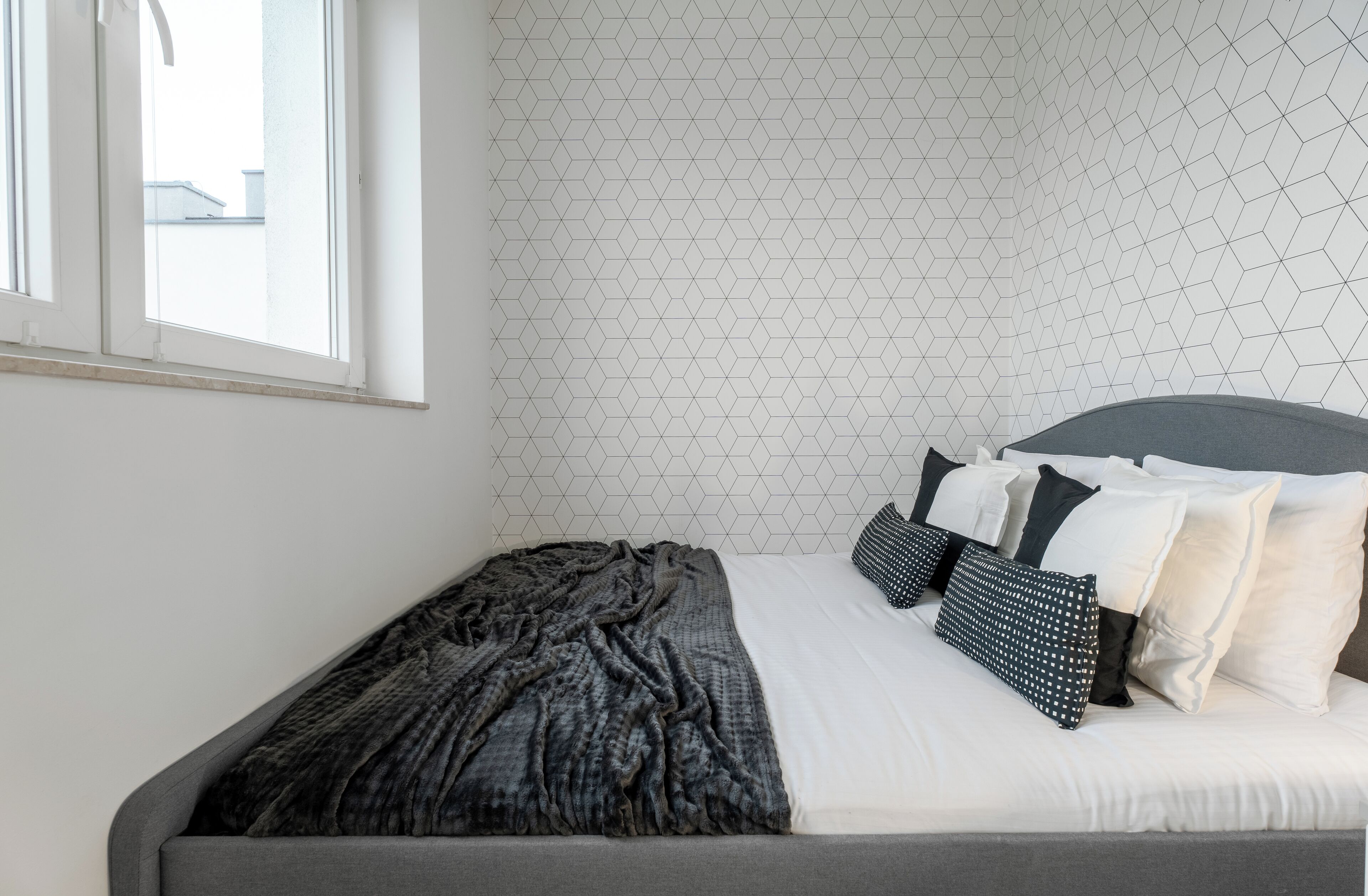 A neatly made bed with a grey headboard, white bedding, and several black and white pillows.