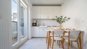 A modern kitchen with white cabinets, a dining table with chairs, and a view of the outside through large windows. - Pure Rental Premium Inżynierska (Wrocław)